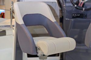 Close-up of a grey padded boat helm seat with a steering wheel in the background. Boat helm seats are designed to provide comfort and support for the captain while operating the vessel.